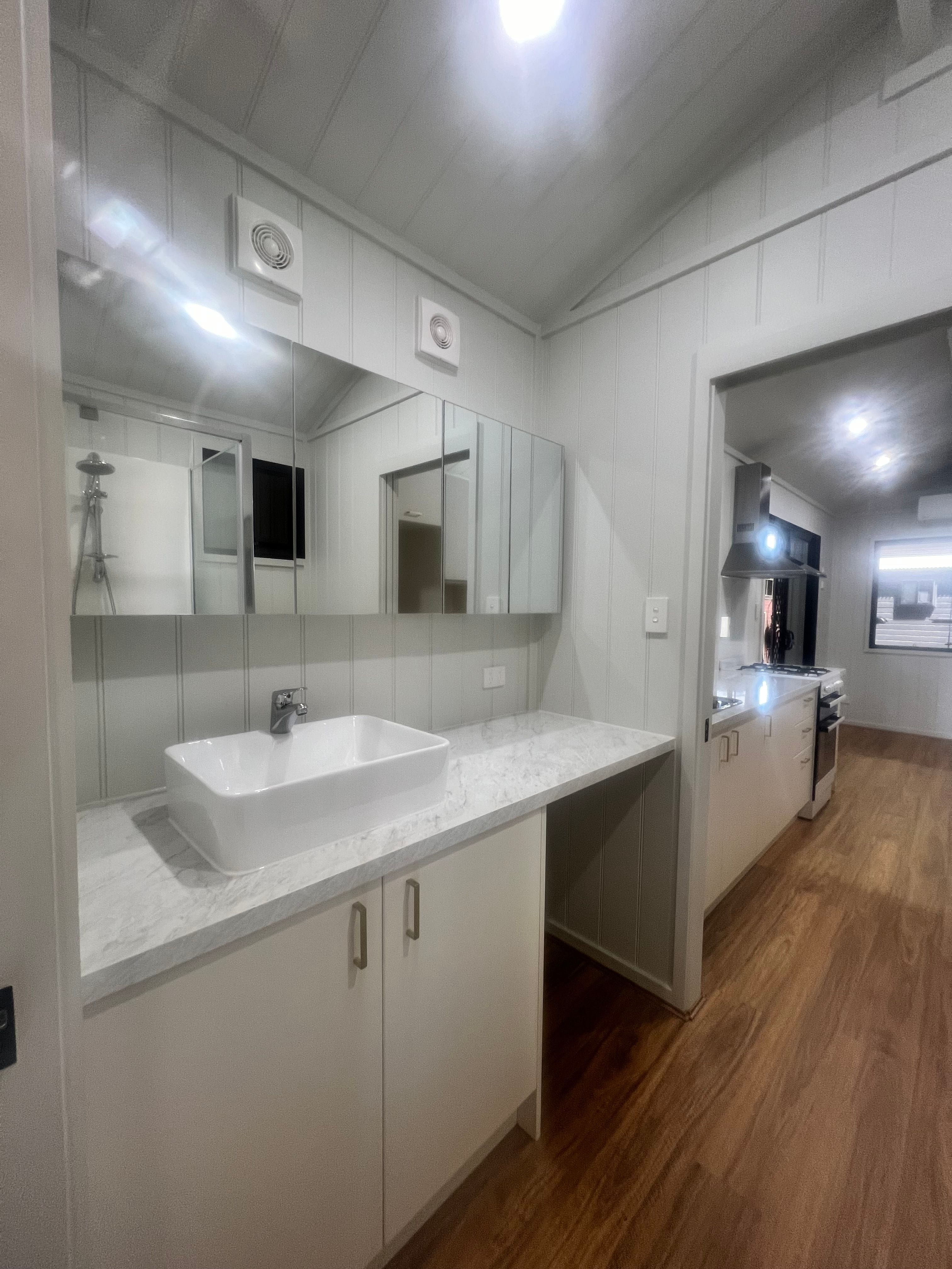 View of the stylish bathroom flowing into the kitchen and living area of the Tiny Grandeur tiny house on wheels